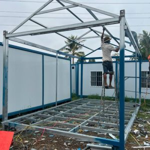 Technicians welding heavy-duty galvanized steel frame and pitched roof trusses for container classroom fabrication.