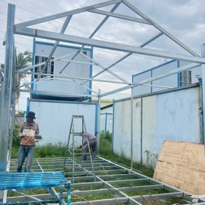 In-house welding of structural steel base grid and roof frame for modular school container units.