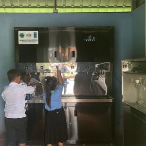 Cambodian school children using touch-button smart drinking water purification station with digital temperature display.