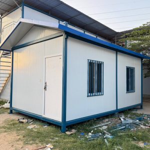 Fully assembled white and blue insulated container classroom with security window bars and weatherproof pitched roof.