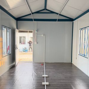 Interior view of container classroom showing open entrance door, security bar windows, wall power switches, and electrical conduit setup.